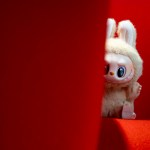 Labubu toy looking out behind a couch