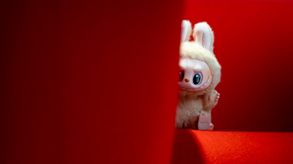 Labubu toy looking out behind a couch